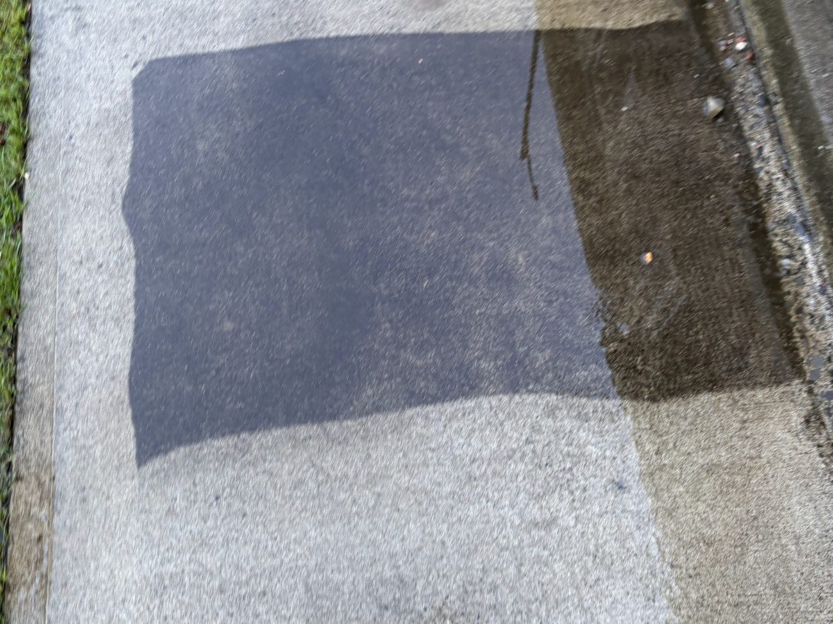 A concrete pad halfway through pressure washing: one clean stripe down the middle of the dark concrete