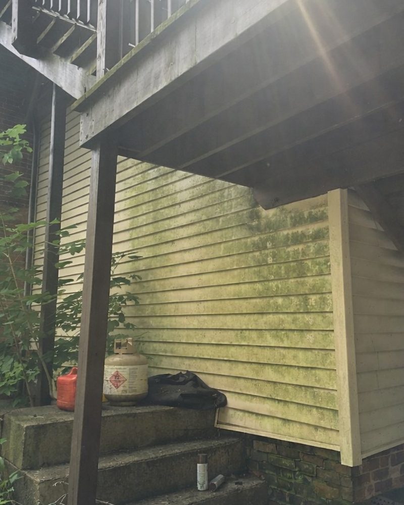 Yellow siding under a deck, streaked green